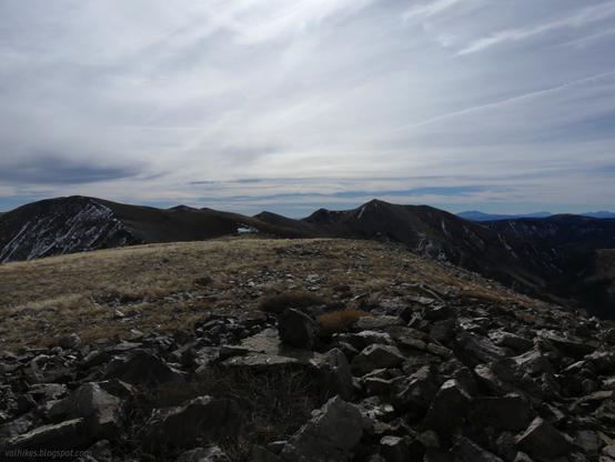 Looking south to Taft Peak (left) and South Schell Peak (right) in the High Schells Wilderness, Humboldt-Toiyabe National Forest, Nevada.
 
A wide, flat, rocky ridge top dominates the foreground covered only with a little dried grasses. The ridge continues, rocky, off to the left to a rise, then along many small rises to the right and a second, pointy, rise, then flatter on further to the right and distance. Thin lines of snow are seen dropping down the more sheltered faces of this above tree line ridge. A little of the valley is seen to the right, with lots of green trees in the bottom.