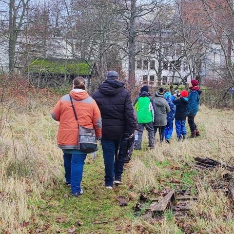 Kinder und Erwachsene im Naturfreundegarten auf der suchte nach Beobachtungsplätzen. Menschen auf einem Rasenweg.