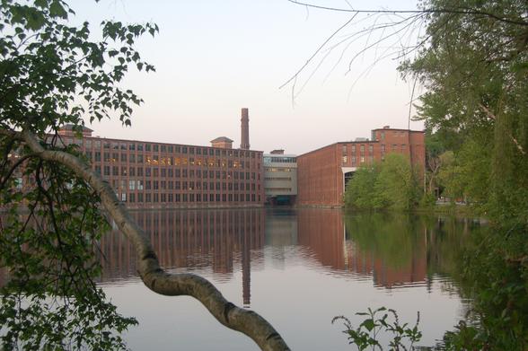 A still evening in Maynard Massachusetts, viewing the structures of a brick woolen mill (and former headquarters of Digital Equipment Corporation) reflected upon the still waters of the millpond, framed through some trees.

Invisible in the photo near the left building submerged in millpond is a trestle from an old shortline train that once entering the millyard through the gap under the bridge at the center of the image. The remains of the trestle are now only visible during times of drought.