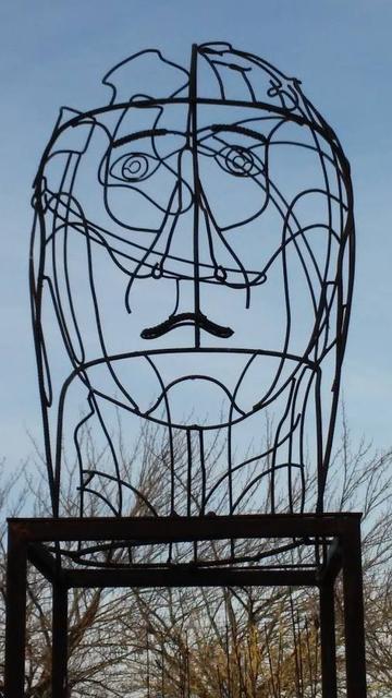 Kunstwerk auf dem Jerg-Ratgeb-Skulpturenpfad in Herrenberg aus Draht das einen Kopf darstellt. Im Hintergrund sind Äste und Himmel zu sehen.