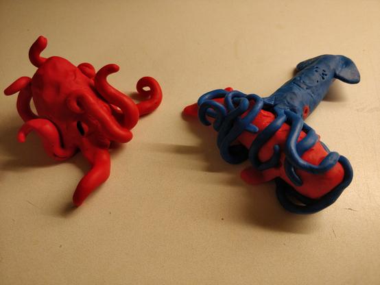 A huge octopus is watching as a sperm whale is being devoured by a giant squid.

The octopus is red, with all its tentacles raised in intricate shapes. A single eye with a slitted black pupil can be seen.

The squid is blue, with large red, round eyes. It has all of it's ten tentacles wrapped around a red sperm whale. The whale is about the same size as the squid, not counting the arms.