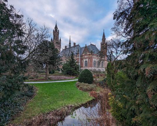Peace palace building in the background, in the foreground the garden with shrubs and a small stream