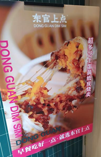 A sign advertising freshly steamed Shanghai-style shaomai sticky-rice dumpling with salted egg yolk and cheese. The food photography shows the cheese stretching as the shaomai is pulled apart.