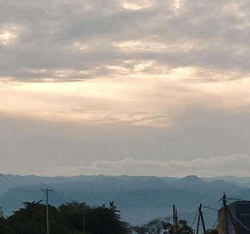 Gros plan sur le ciel au dessus des collines. Il est très nuageux; le soleil couchant donne différentes couleurs du blanc au gris en passant par le jaune très pâle...