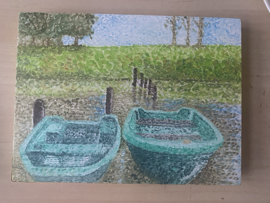 A small landscape-orientation watercolour painting on a cradled panel, sitting on a desk. It is a pointillism-style painting, made up of many dots of colour. The painting depicts two teal rowing boats moored at the ender of a boating lake. There is green grass, trees and blue sky on the far side of the lake.