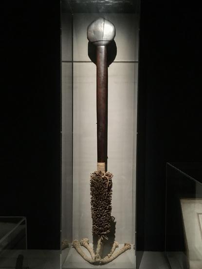 Longue massue en bois, dont la poignée est garnie d’un manchon de coton d’où pendent de grosses franges, jadis couvertes de plumes.