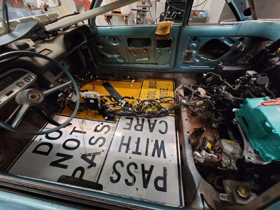 The stripped interior of a 1964 Corvair with street signs for floor panels and a wiring harness strewn about