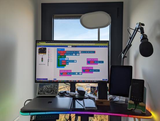 Standing desk with a NeoPixels strip running around it that displays a rainbow gradient. The screen shows the block code.