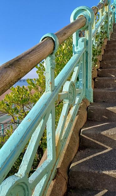Old and partly rusting stair railings on Brighton seafront. Light cyan colour metal with wooden handrails looping through the frames at the top