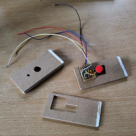 a self-built Raspberry Pi interface with a pushbutton and an LED soldered to some pullup and current limiting resistors, positioned on a plotter-cut cardboard case