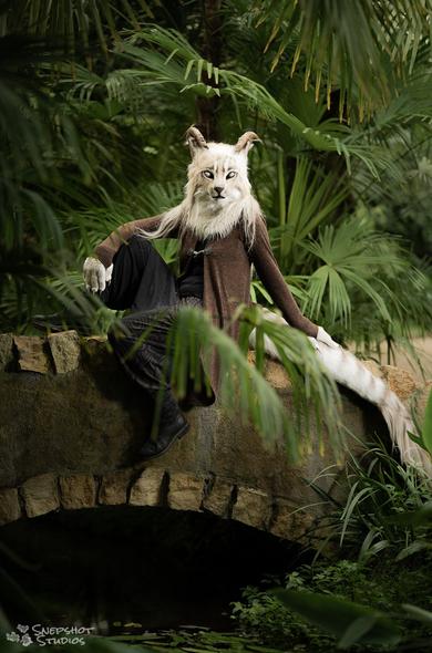 Realistic Orahier fursuit sitting on a small stone bridge surrounded by deep green palm trees