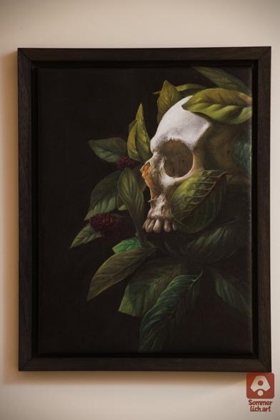 Oil painting of a skull which is surrounded by green leafs