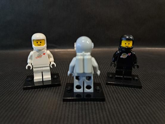 L'origine de la figurine grise ?

Trois figurines LEGO, du thème "Space". Devant et au centre, floue, une grise. Elle est de dos pour qu'on voit ses bouteilles d'oxygène. Derrière, nettes, une blanche à gauche et une noire à droite.