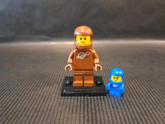 Deux figurines LEGO, du thème "Space". Une brune, taille normale et un bébé en combi spatiale bleue. Elles sont côte à côte.