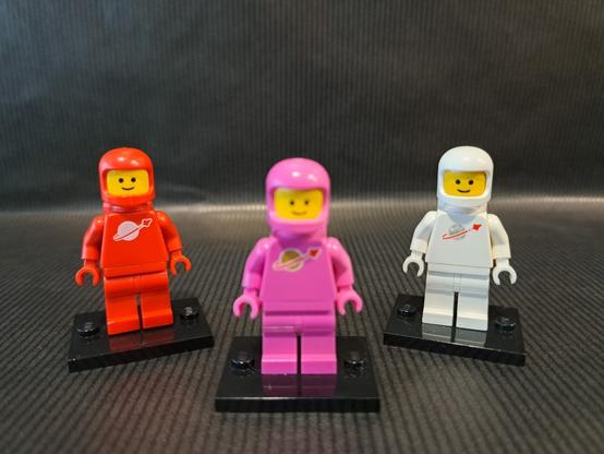 L'origine de la figurine rose ?

Trois figurines LEGO, du thème "Space". Devant et au centre, floue, une rose. Derrière, nettes, une rouge à gauche et une blanche à droite.