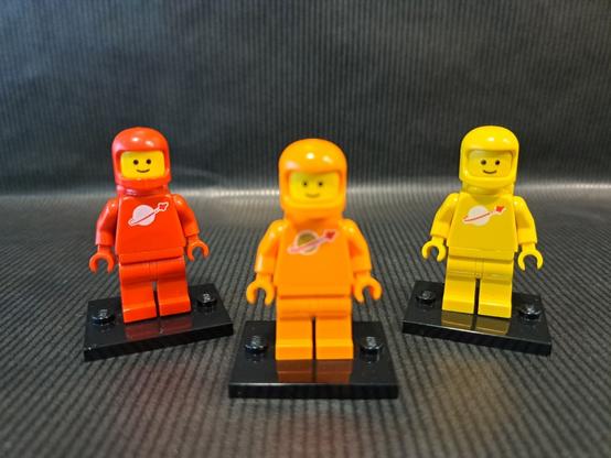 L'origine de la figurine orange ?

Trois figurines LEGO, du thème "Space". Devant et au centre, floue, une orange. Derrière, nettes, une rouge à gauche et une jaune à droite.