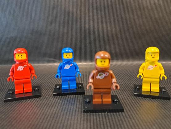 L'origine de la figurine brune ?

Quatre figurines LEGO, du thème "Space". Devant, floue, une brune. Derrière, nettes, une rouge tout à gauche, une bleue et une jaune à droite.