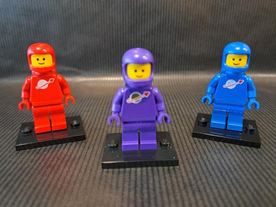 L'origine de la figurine violette ?

Trois figurines LEGO, du thème "Space". Devant et au centre, floue, une violette. Derrière, nettes, une rouge à gauche et une bleue à droite.