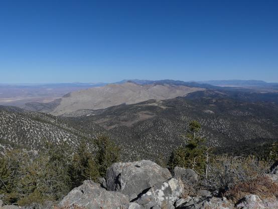 North view from the top of the high point of South Egan Range Wilderness, Nevada

A few rocks in the foreground top a steep slope that a few distant trees can be growing on. (They are pines.) Further, hills roll away covered in thin juniper. Past that, a peak covered in tan of sagebrush and dried grasses rises to a line of points that happen to contain one almost as high as here. More mountains are beyond.