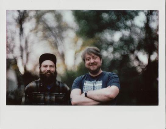 An Instax Wide instant photo of two men looking at the camera, majorly out of focus in the background with swirly highlights.