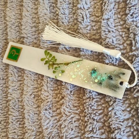 FFXIV long rectangular bookmark, Green Whitemage label, white tassels. Pearl-white majority body with green leaves, aqua glitters, and black ground gravel embedded
