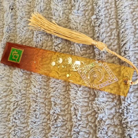 FFXIV long rectangular bookmark, Green Astrologian label, gold tassels. Gradient dark amber to light yellow translucent majority body with moon glitter, silver dust , and laser card insert.