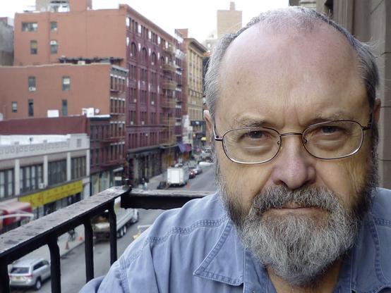 A self-portrait photo of Phill Niblock sitting on an old fire escape in New York City, circa 2013.