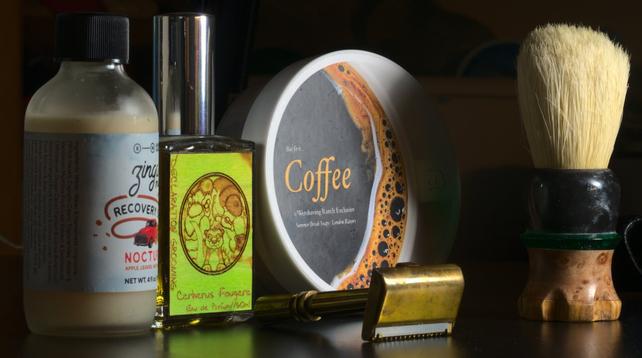 A brass EldrormR Industries MM24 razor with a Chisel and Hound brush with Zenith boar knot in front of a tub of SBS/LR Coffee soap, a bottle of Z/BaM Nocturne toner, and a bottle of HoM/NO/DG