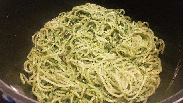 Espaguetis con la salsa de pesto sofriéndose en un cazo.