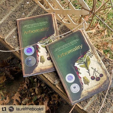 A photo of two copies of Arboreality by Rebecca Campbell, on a brick border with a tangle of vines. From the @laurelthebooks Instagram account.