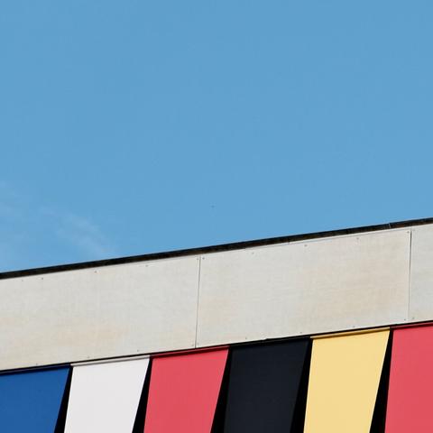Edges of modern buildings featuring striking patterns of primary and secondary colored panels against the backdrop of a clear blue sky.