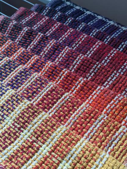 handwoven huck fabric in a rainbow gradient laid on a drying rack. the fabric transitions from bright yellow in the bottom right corner to deep purple in the top left