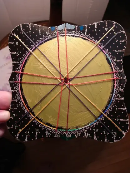 a kumihimo disk with 16 strands of embroidery floss in four colors arranged on top