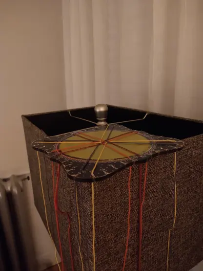 the same disk resting atop a square lampshade, threads hanging down
