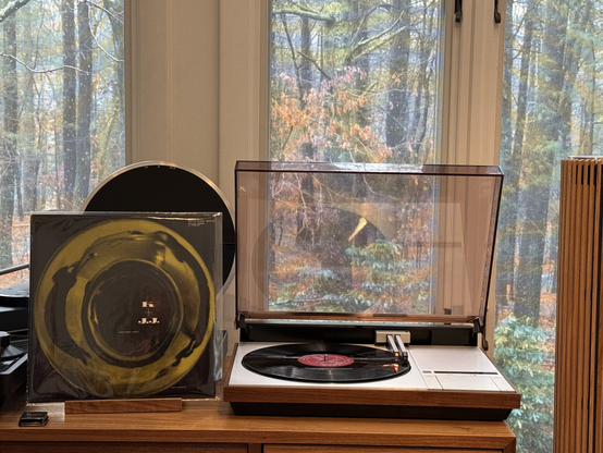 Kai Winding and J.J. Johnson - K + J.J. LP cover.

The bell of a Trombone shot head-on against a black background. The two leaders are shown distorted and reflected in the bell.

The black LP plays on a vintage Bang & Olufsen Beogram 4000 linear-tracking turntable to the right. The dustcover is open, and the album, tonearm and surround are reflected in its underside.