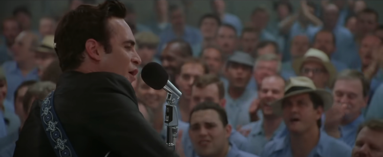 A man plays guitar on a stage in front of a group of male prisoners