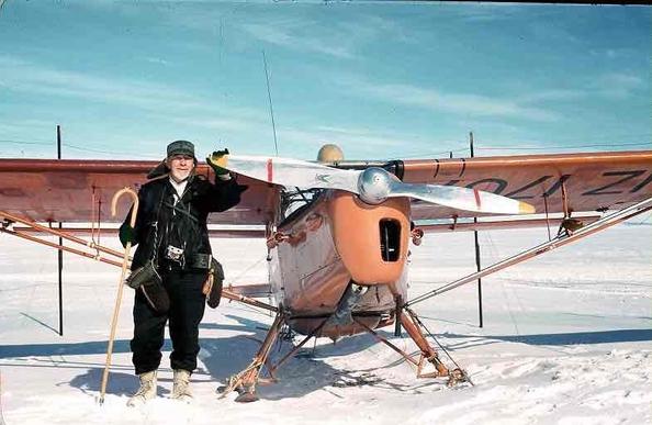 A man standing next to a small airplane in the snow.