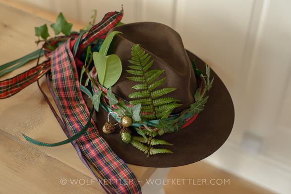 A brown felt hat on a wooden table. The hat is decorated with fabric ribbons and greenery.