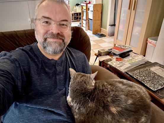 Me, sitting on my couch, with a cat (Lucy) lying simultaneously on the armrest and me.