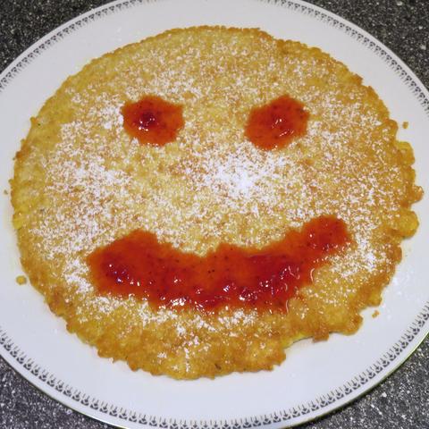 Auf einem Teller liegt ein Eierkuchen mit einem aufgemalten Gesicht aus Erdbeersoße