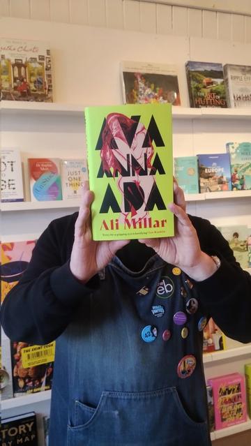 Bookseller Joe holding up a copy of Ava, Anna, Ada, a debut novel by Ali Millar, to recommend it in the Edinburgh Bookshop
