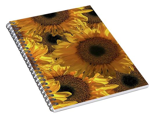 A spiral notebook with sunflowers on the cover. The notebook is lying at angle so the spiral and thickness is visible.