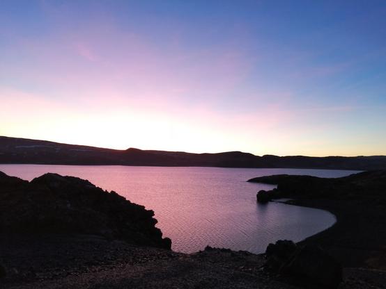 Une partie du lac Kleifarvatn sur lequel se reflète la couleur du ciel avec des teintes roses et mauves.