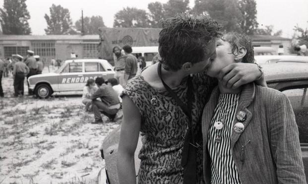 Two young people, wearing punk badges, kiss passionately. In the background people mill around. And there is a Police car too, along with several policemen, keeping an eye on things.