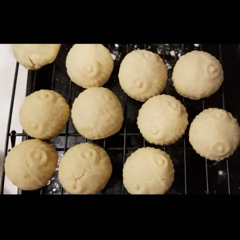 A dozen naked ma'amoul cooling on a wire rack. Naked equals without powdered sugar on top.