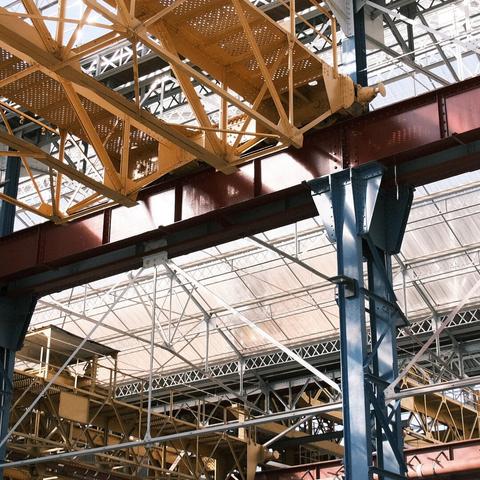The sturdy intersection of yellow and red steel girders against a complex backdrop of blue beams and translucent roofing.