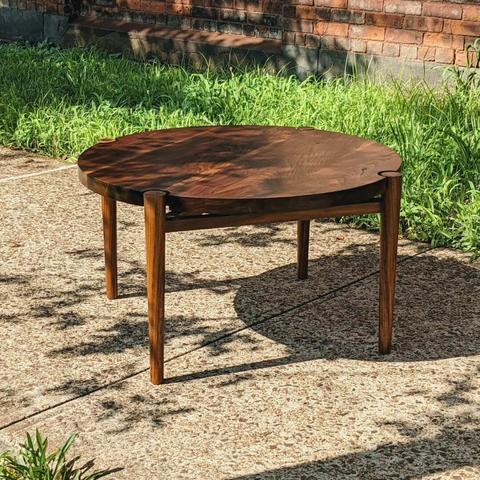 A circular walnut coffee table takes in the sun on a grass lined sidewalk.