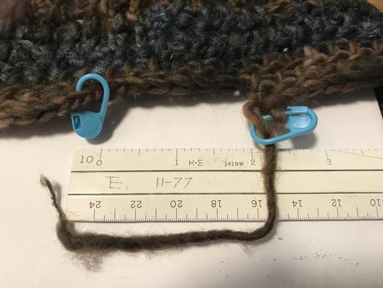 The last few rows of a brown & gray crocheted hat/beanie/toque. The final row is unfinished, with a small gap between the last stitch and the start of the row where it needs to meet. A bedraggled little tall of yarn, too short for much of anything, curls around a scale showing that that gap is a frustratingly small two inches (about 50 mm). *nb: please feel free to ignore the weird upside-down  markings at the bottom of the scale).
Technical notes in crochet-ese (US notation): last row was done in hdc with an H hook, will  frog  & redo in sc w/ H hook. Preceding rows are all hdc: brown with I hook, gray with J hook. Brown is a  slubby variegated yarn from a grab bag somewhere, 4/5 worsted/aran, probably acrylic. Gray is a bulky gradient nylon yarn I forget the name of. Pattern is off the top of my head/from the seat of my pants.