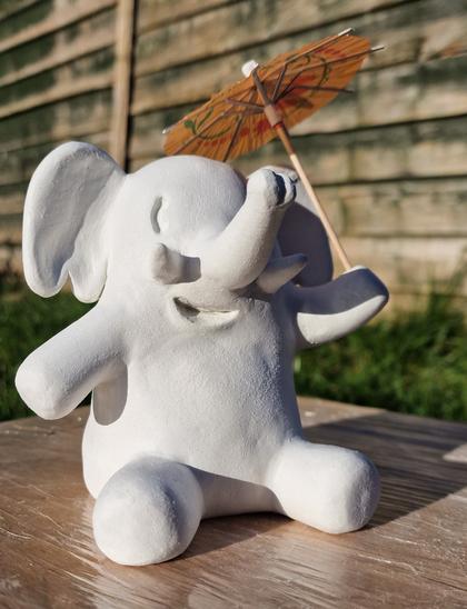 Clay model of the mastodon elephant mascot sitting down and holding a cocktail umbrella