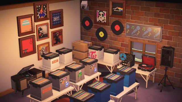 Animal Crossing: New Horizons screenshot. Interior of a room intended to look like a record store. The left wall is white paint and the back / right wall is brownish brick. Both walls have framed albums on the wall from K.K. Slider as well as custom designs to look like album covers from artists like Psy, 2NE1, Trident, and Goldfinger. Along the left wall is a table with boxes of records and an old fashioned record players set up. On the back / right wall are two tables with records and a record player / sound equipment. Between the two walls are stacked cardboard boxes. In front of the two tables are two rows of two white tables with boxes of records. The floor is grey with two record-like rugs. On the back, brick wall there are also what appear to be three records attached to the wall.